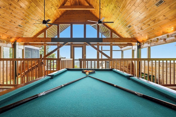 A pool table in a room with wooden beams and large windows.