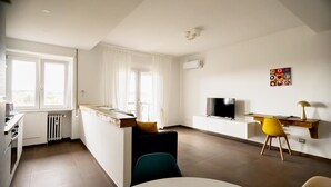 Eine moderne Wohnung mit Küche, Essbereich und Wohnraum. Sie beinhaltet einen Fernseher, einen Esstisch und ein Sofa.