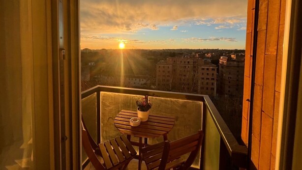 Ein Balkon mit Tisch und Stühlen mit Blick auf eine Stadtlandschaft bei Sonnenuntergang.