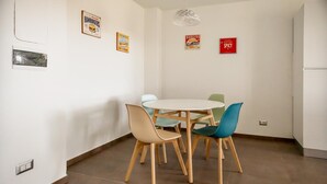 Ein Essbereich mit einem runden Tisch, vier Stühlen, einer Pendelleuchte und Wanddekorationen, darunter Schilder mit 'Hamburgers' und 'Hot Dogs'.