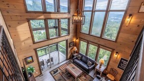 A spacious loft-style room with large windows offering views of a forested mountain range. - New Lux 4 King Suites | Hot Tub | Game Rm | PS5 (Gatlinburg)