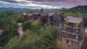 A modern multi-story building with balconies, surrounded by lush greenery and mountains in the background. - New Lux 4 King Suites | Hot Tub | Game Rm | PS5 (Gatlinburg)