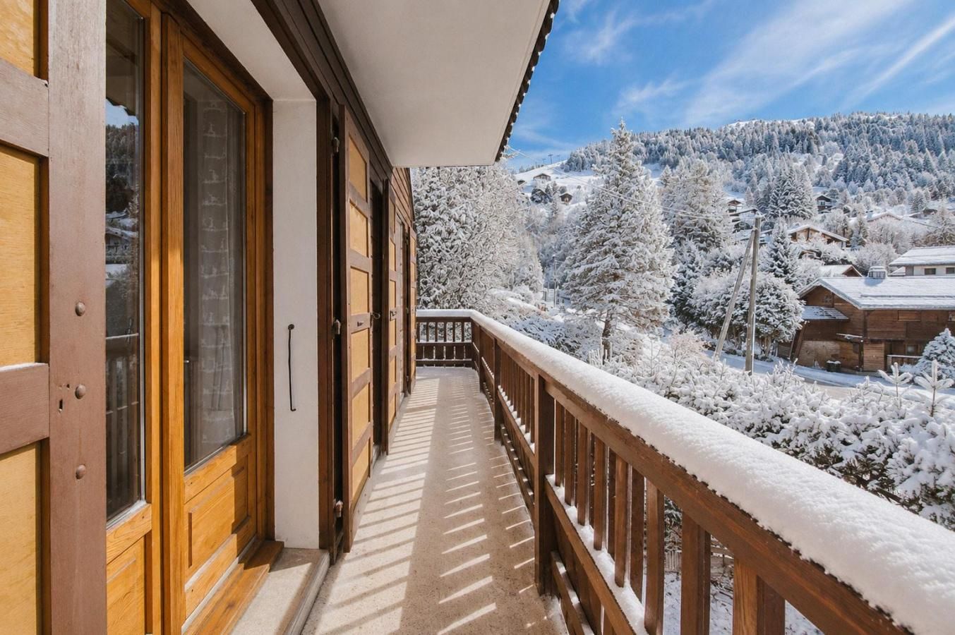 A wooden balcony with a view of snow-covered trees and houses.