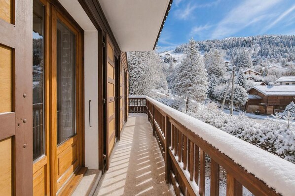 A wooden balcony with a view of snow-covered trees and houses.