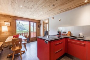A modern kitchen with red cabinets, a central island, and a dining area with wooden furniture.