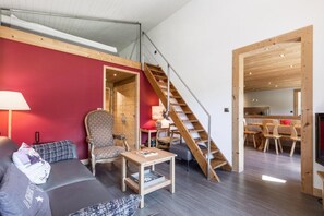 A modern living room with a red accent wall, a wooden staircase, and a dining area with wooden furniture.