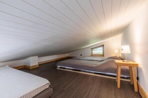 Ein kleiner Raum mit geneigtem Dach, zwei Betten, einem Fenster und einem Nachttisch mit Lampe.