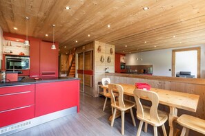 A modern kitchen with red cabinets, wooden ceiling, and a dining area with wooden chairs and a table.