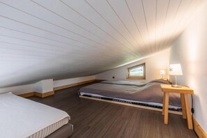 A small, sloped-roofed room with two beds, a window, and a bedside table with a lamp.