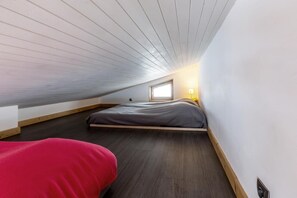 Ein Zimmer mit schrägen Wänden, einem Bett, einem Fenster und einem roten Sessel.