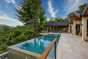 Une maison moderne dotée d’une piscine, d’un espace salon extérieur et offrant une vue sur la forêt.