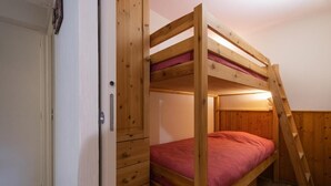 Un lit superposé avec une échelle en bois, une porte et un petit meuble à tiroirs.