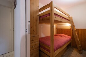 Uma cama beliche com escada de madeira, uma porta e um pequeno conjunto de gavetas.