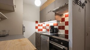 Une cuisine compacte avec une table en bois, des appareils en acier inoxydable et un dosseret à carreaux rouges et blancs.