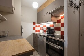 Cozinha compacta com mesa de madeira, eletrodomésticos de aço inoxidável e painel de fundo xadrez vermelho e branco.