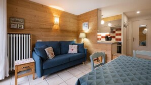 Une pièce chaleureuse avec un canapé bleu, une petite table, une chaise et un lit recouvert d’une courtepointe matelassée.