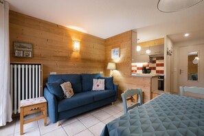 Quarto aconchegante com sofá azul, uma mesinha, uma cadeira e uma cama com cobertura acolchoada.