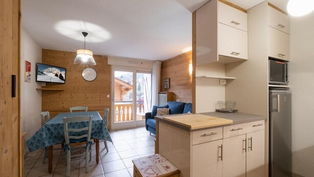 Une cuisine compacte avec un coin repas, des murs en bois et une vue à travers une porte vitrée.