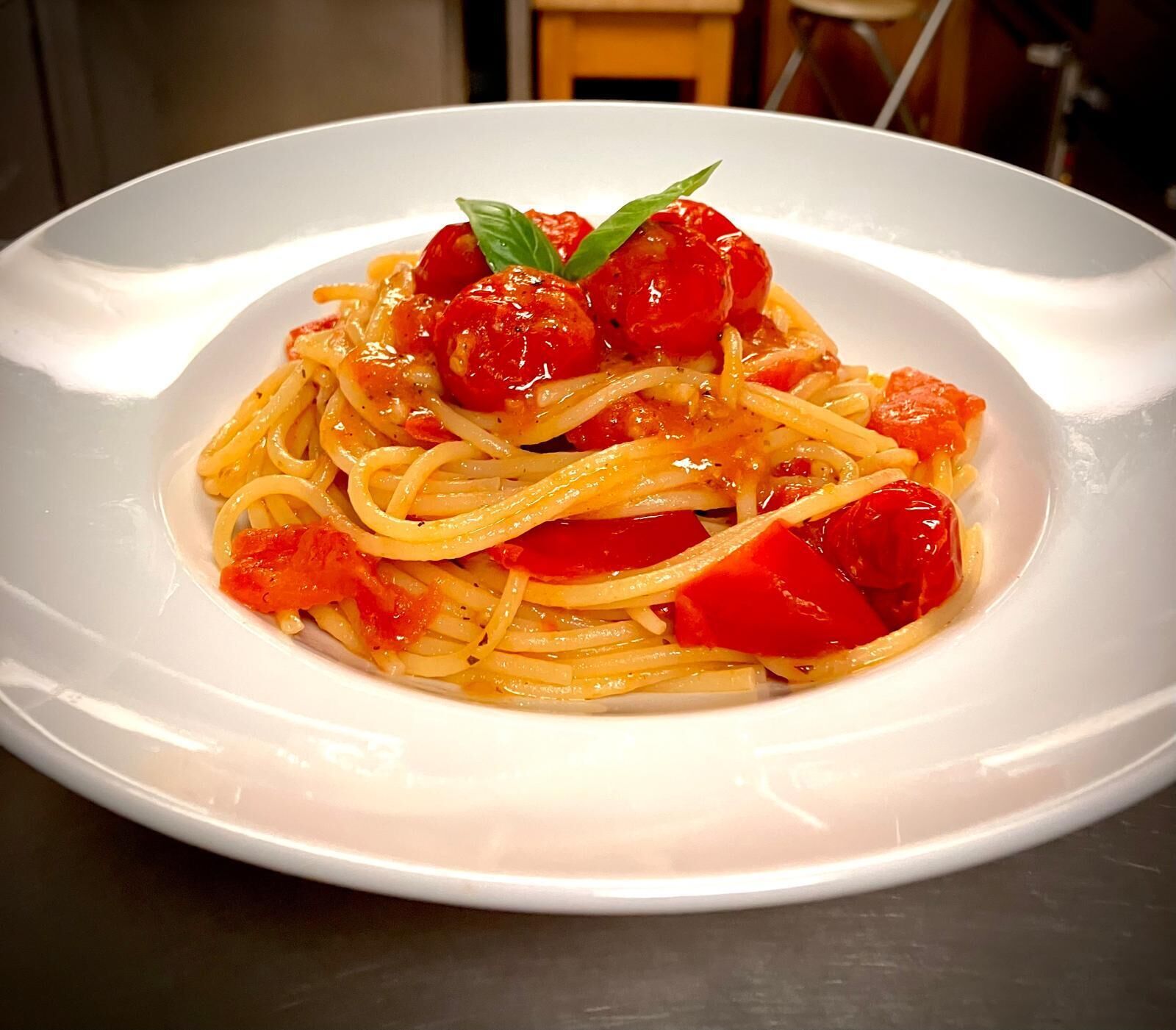 Une assiette de spaghettis avec des tomates cerises et une feuille de basilic.
