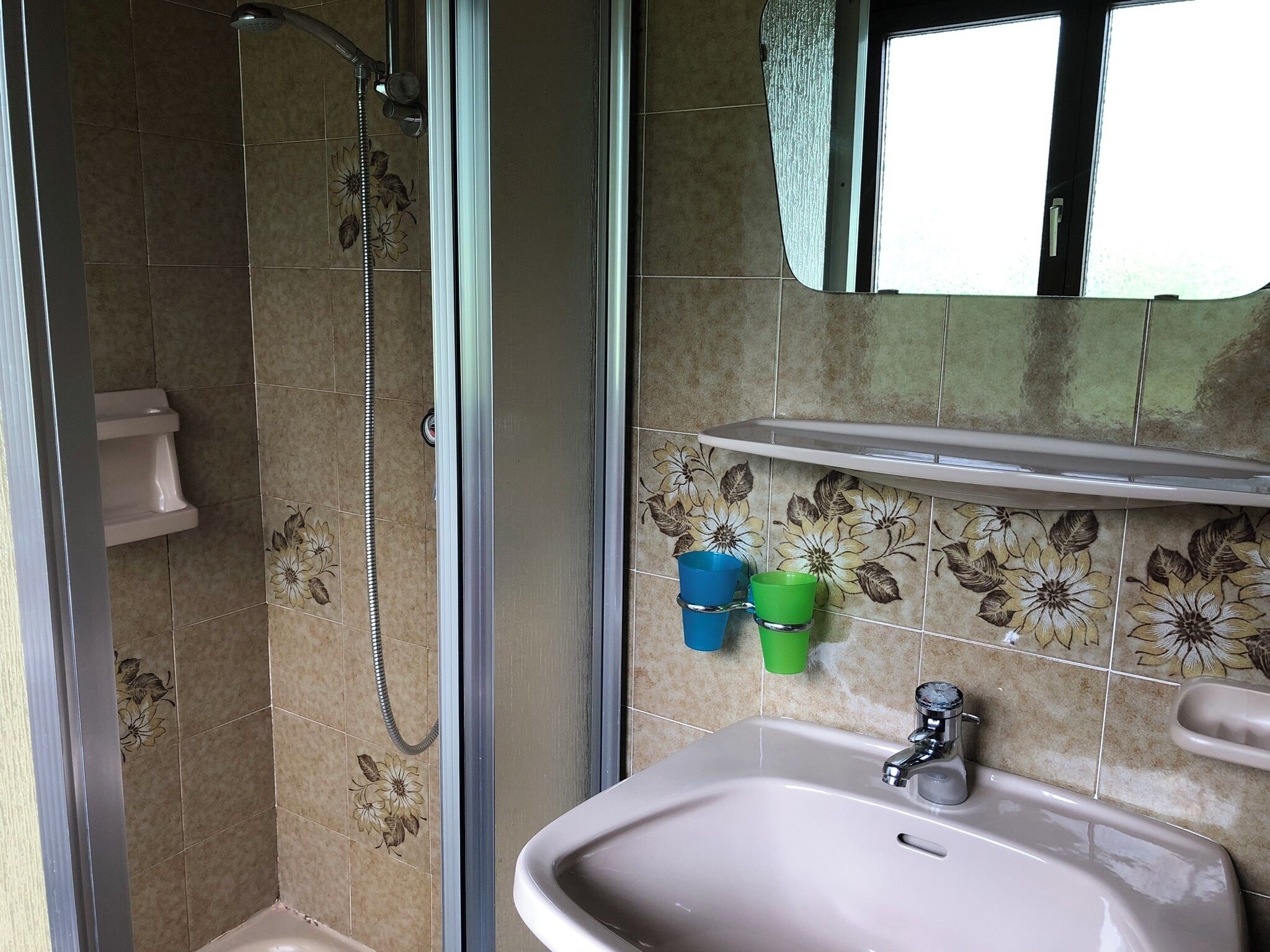 A bathroom with a shower, sink, and a shelf with two cups.
