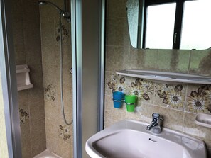 A bathroom with a shower, sink, and a shelf with two cups. - Gasthof Rösslhof (Goldegg)