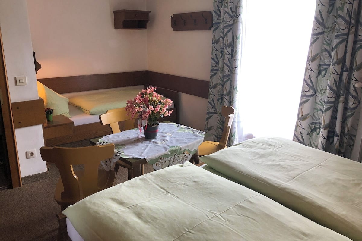 Una habitación acogedora con una cama, una mesita con una planta en maceta, una silla y un banco.