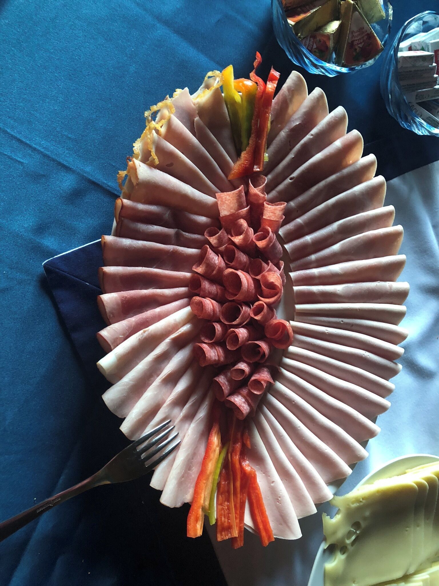 A plate of sliced meats and vegetables arranged in a circular pattern on a blue tablecloth.