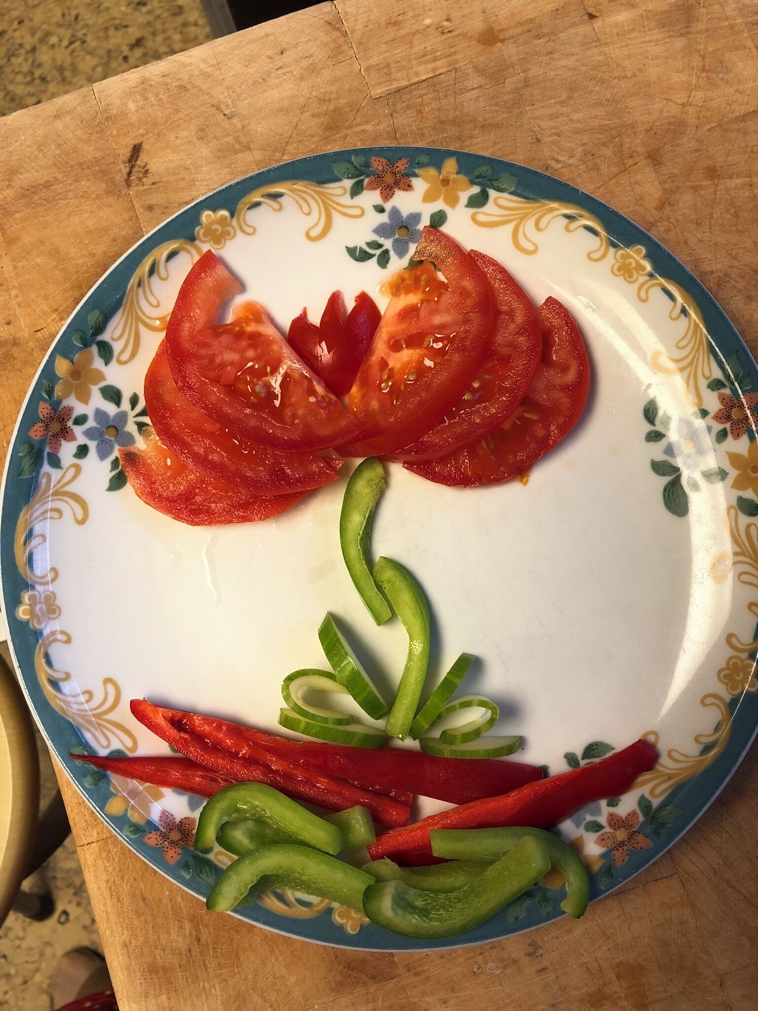 Ein Teller mit floralem Muster und Tomatenscheiben, die eine Blume bilden.
