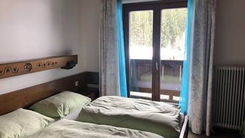 A bedroom with a wooden headboard, two beds with green bedding, a window with blue curtains, and a view of a deck outside.