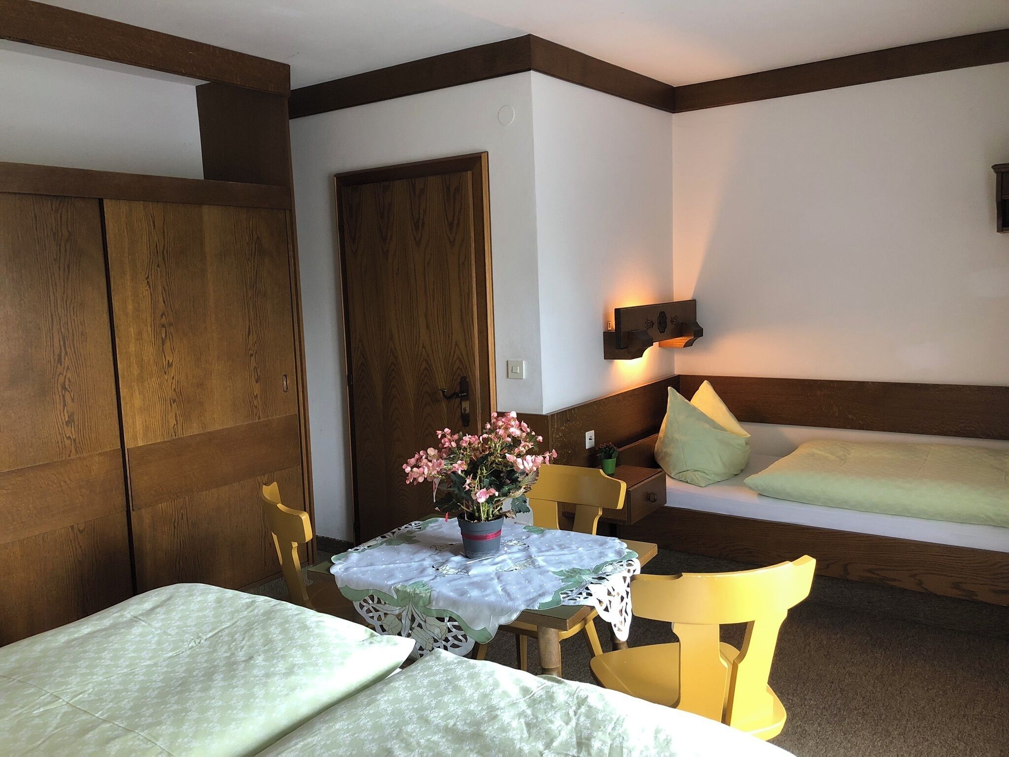 A room with a bed, a table with a flower vase, and a chair.