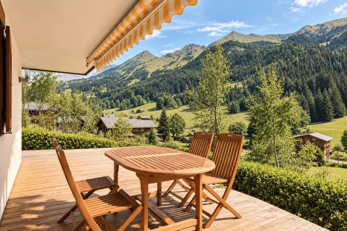 A wooden deck with a table and chairs, overlooking a mountainous landscape with houses and greenery.