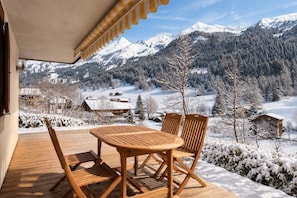Um deck de madeira com mesa e cadeiras, com vista para uma paisagem montanhosa coberta de neve.