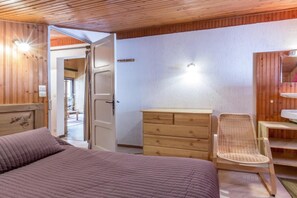 A bedroom with a bed, wooden dresser, wicker chair, and a bathroom with a mirror and sink.