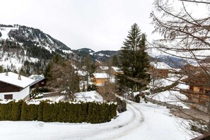 A snow-covered mountain village with wooden houses, a winding road, and a prominent evergreen tree.