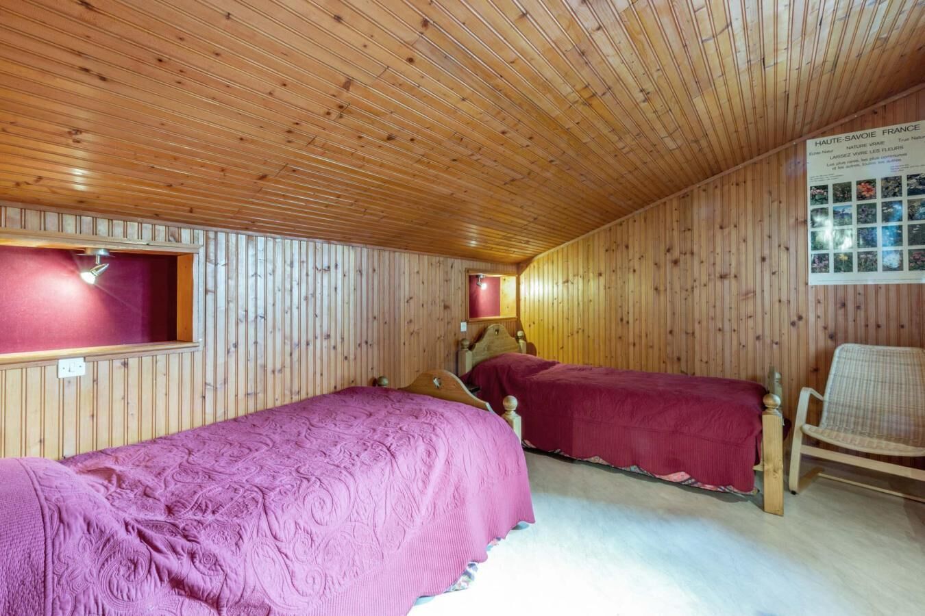 A room with wooden paneling and two beds with red bedding.