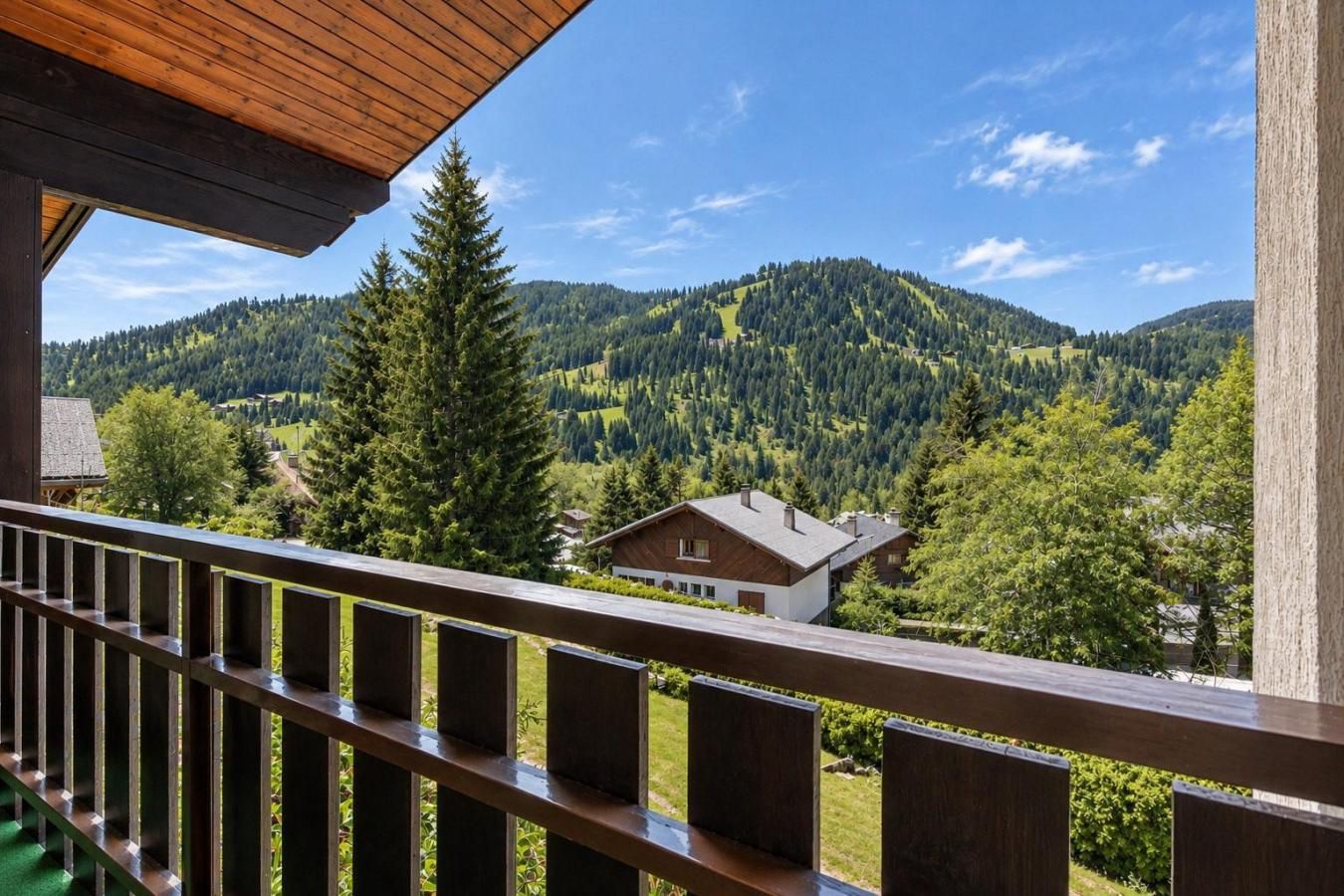 A wooden balcony with a view of a mountain landscape, a house, and a clear sky.