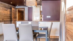 Uma sala de jantar com parede de madeira, mesa de vidro e quatro cadeiras.