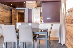 Un coin repas avec un mur en bois, une table en verre et quatre chaises.