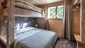 Quarto de cabana de madeira com beliche, janela com cortinas e escada.