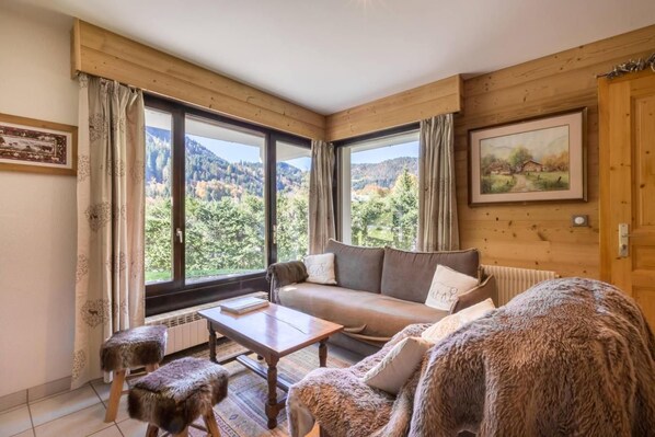 A cozy room with a sofa, a table, and a view of the mountains through large windows.
