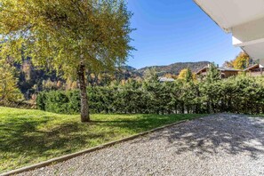 A gravel path leading to a building with a view of a forested hillside and houses in the background.
