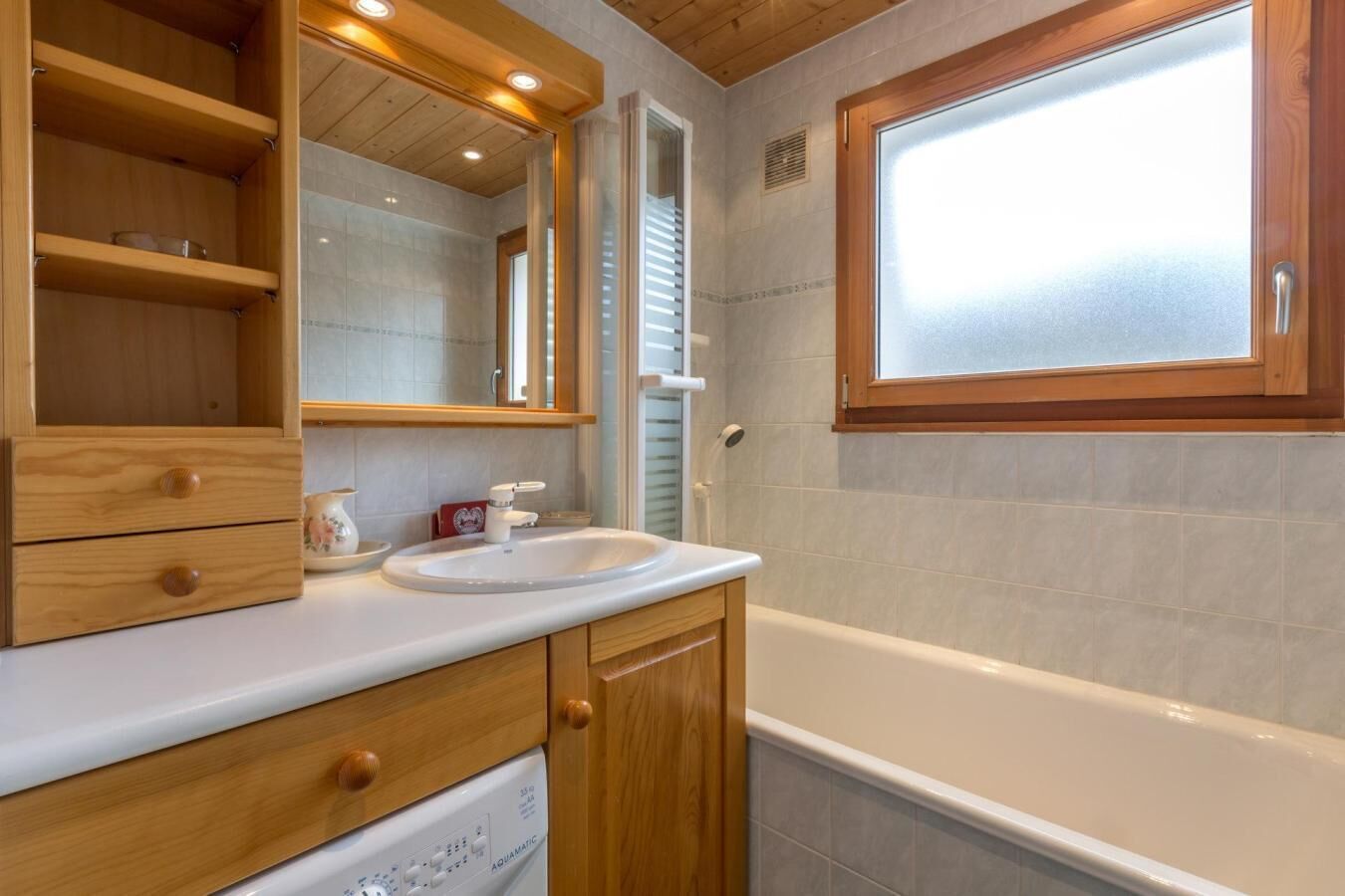 A bathroom with a wooden vanity, a white sink, a mirror, a window, and a bathtub.