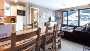 A modern kitchen with a microwave, coffee maker, and a dining area with wooden chairs and a table. There is a sofa and a large window with a snowy view.