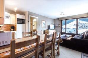 A modern kitchen with a microwave, coffee maker, and a dining area with wooden chairs and a table. There is a sofa and a large window with a snowy view.
