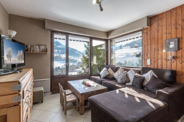 A modern living room with a large window, a flat-screen TV, a sofa, a coffee table, and a wooden cabinet.