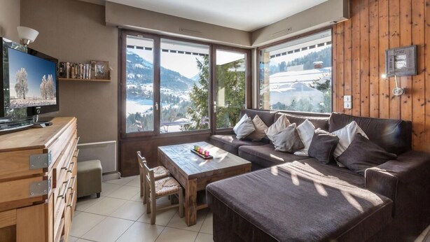 A modern living room with a large window, a flat-screen TV, a sofa, a coffee table, and a wooden cabinet.