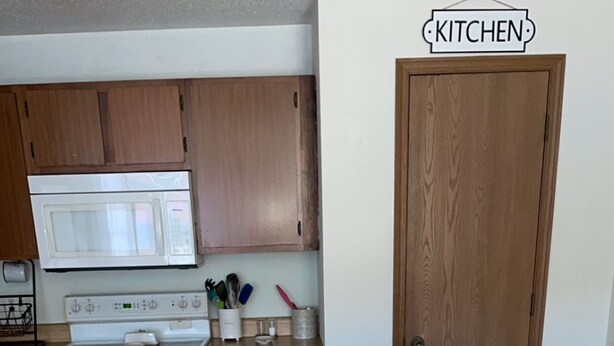 A kitchen with wooden cabinets, a white stove, a microwave, and a wooden door. There is a calendar on the wall and a tissue box on the counter. - Grant City Nightly Rental

 (Grant City)