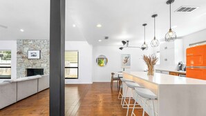A modern kitchen with a stone accent wall, a bar area with white stools, and pendant lighting. - Close to Domain,DT,Shopping | Chic & Serene | 3BR (Austin)