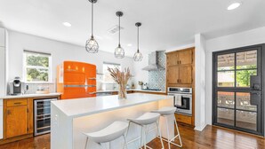 A modern kitchen with a central island, bar stools, pendant lights, and a large window. - Close to Domain,DT,Shopping | Chic & Serene | 3BR (Austin)