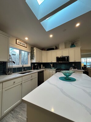 A modern kitchen with a skylight, white cabinetry, and a central island with a glass bowl.